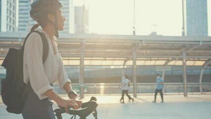 Asian businesswoman go to work at office walk and smile wear backpack look around take bicycle on street around building on a city street. Bike commuting, Commute on bike, Business commuter concept.