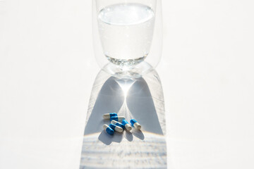 Colorful pills in the shadow of the glass with water.
