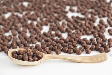 Chocolate corn balls in a wooden spoon scattered on a white background. Top view. Copy, empty space for text