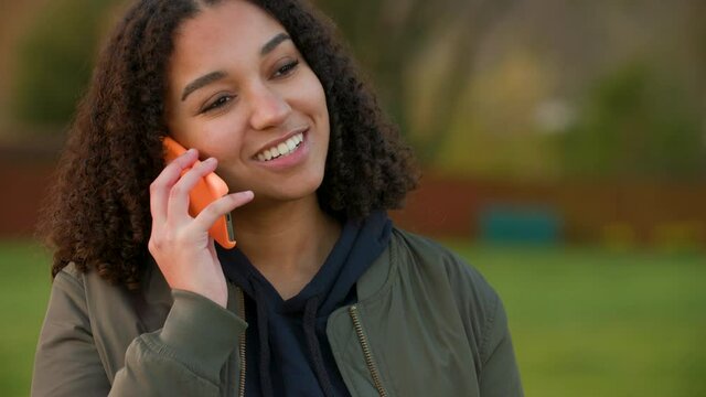 Beautiful, happy, smiling mixed race African American girl teenager young woman outdoors talking on her smartphone or cell phone