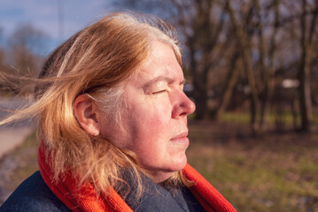 Woman with closed eyes,  red scarf and blue jacket enjoys the sun rays