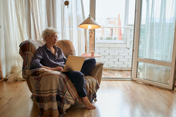 Active age ageless elderly woman working from home on a laptop