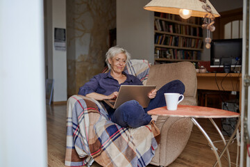 Active age ageless elderly woman working from home on a laptop