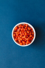 sea buckthorn berries in a white plate on blue background. healthy food concept