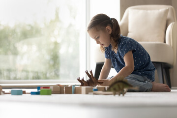 Small Caucasian girl child sit on floor in living room play with animal figures on weekend. Cute little 8s kid have fun relax alone at home, involved in playful game activity. Entertainment concept.