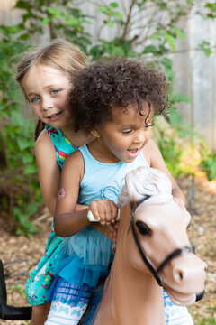 A young girl and her toddler friend riding on the back of a toy horse together.