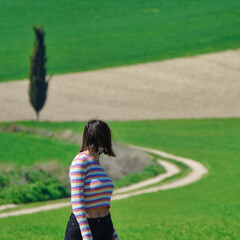 Young short hair brunette woman seen from behind walking on a path in the green field