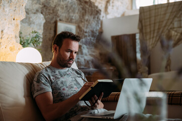 Young man working with laptop and taking notes in notebook at home