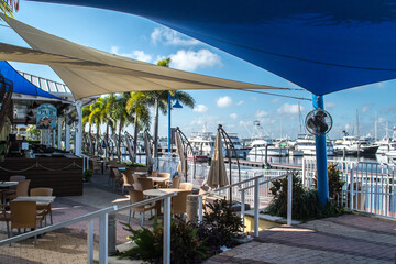 Downtown historic Stuart, Florida. Restaurants on the St. Lucie River with outdoor eating areas covered with blue awnings, yachts in the marina, lifestyle at the waterfront town in eastern Florida - obrazy, fototapety, plakaty