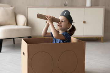 Cute little 7s Caucasian girl child in pirate hat look in spyglass have fun playing at home. Small kid sit in toy ship watch in spy pipe engaged in funny game activity. Entertainment concept.