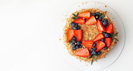 Honeycake with a lot of crunchy crumbs and decorated with strawberries and blueberries. White background. Flat lay
