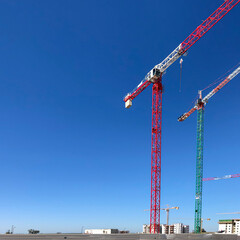 Construction tower cranes on the blu sky background. Houses under construction. Industrial skyline site.