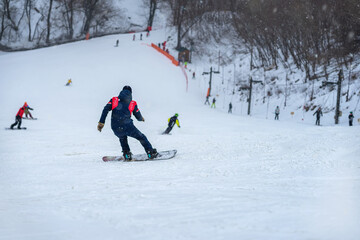 Down slope on snow covered mountain. Back view of snowboarder riding on slope, blurred selective...