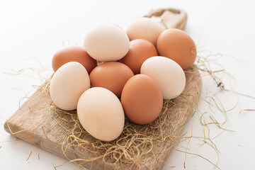 chicken eggs lie on a wooden board in dry grass on a white background. Preparing Easter eggs for the holiday. Light and brown eggs on the Easter table