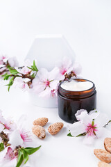 Obraz na płótnie Canvas Jar with cream on a light background. Hand care lotion with almond oil and vitamins. Body skin health and beauty. A bright background, cosmetics and natural almond flowers. Vertical . Mockup