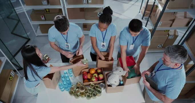 Top view of successful multi-ethnic corporate team volunteers collecting free food and supplies in carton boxes collaborating at workshop.