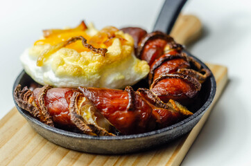 Grilled sausage with onion and egg in a cloud, all served on a cast iron pan