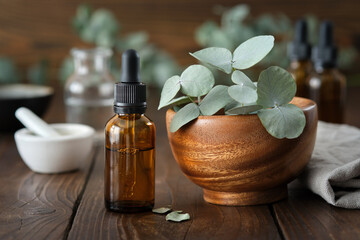 Dropper bottle of eucalyptus essential oil and wooden bowl of green eucalyptus leaves. Mortar and...