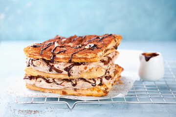 Puff Pastry square cake with mocha whipped Cream or Chantilly and chocolate drip topping on light blue background, copy space. Selective focus, close-up. Easy celebration desserts concept.