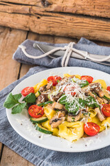 Italian cuisine: Tortellini with vegetarian mushroom cream sauce, zucchini and fresh cherry tomatoes on a rustic wooden table, vertical