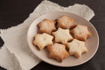 Delicious homemade cookies in the shape of stars sprinkled with sugar. Laid out on a plate on a dark wooden table with a linen napkin.