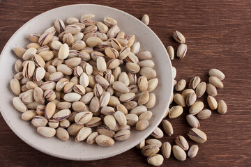 Fried salted pistachios in a light plate on a wooden table