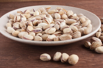 Fried salted pistachios in a light plate on a wooden table