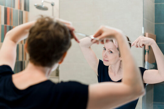 A woman gives herself a haircut at home.