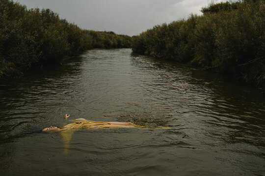 The body of a young beautiful girl in a yellow dress is carried by the river