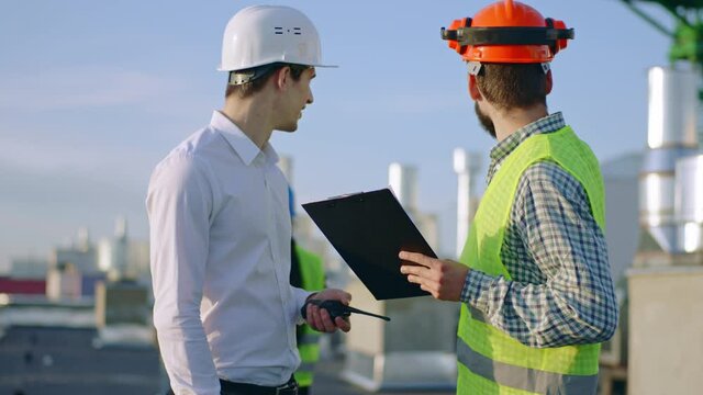 On construction site twi diverse specialists analyzing the plan of construction site using the digital tablet they wearing safety helmets