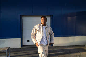 Chico negro apuesto posando delante de una pared azul y puerta blanca