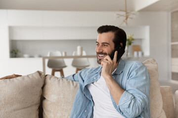 Fototapeta premium Overjoyed millennial Caucasian man relax at home have pleasant cellphone conversation online. Smiling young male talk speak on smartphone call, use wireless good mobile connection. Technology concept.
