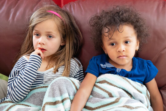 Two children of different races sit together and watch a television programme.