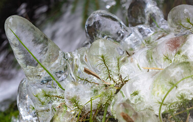 Frozen water close up. Ice waterfall. Transparent ice. Frozen grass, moss and granite stones. Textural ice formations.