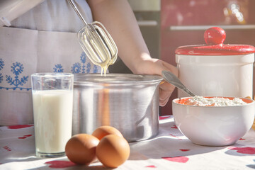 a girl in a white apron makes pancake batter with a mixer in a metal pan