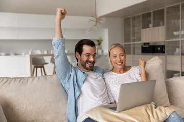 Overjoyed Caucasian couple look at laptop screen feel excited euphoric win online lottery on...