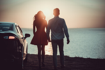 The man and woman walking near the car on the sea shore