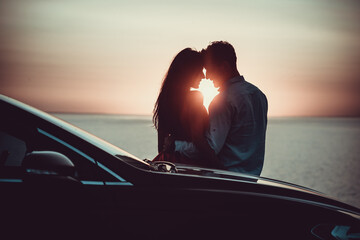 The romantic couple standing near the car on the beautiful sunset background