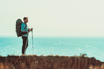 The traveler with backpack standing on the mountain top above the sea