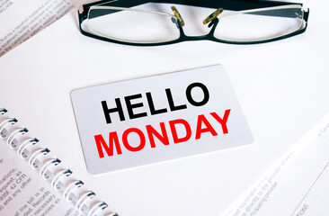 Text Hello Monday on a business card lying on a notepad with eyeglasses and text documents