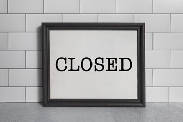 Closed sign on white poster framed with a black picture frame agianst subway tiles no people 