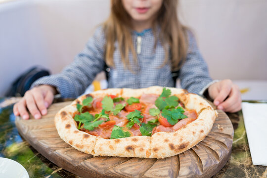 Fototapeta Close-up of  childs hand taking italian pizza on  wooden board in outdoor street cafe. Focus on the foreground.