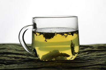 Glass cup with healthy herbal tea on green textile cover with white background