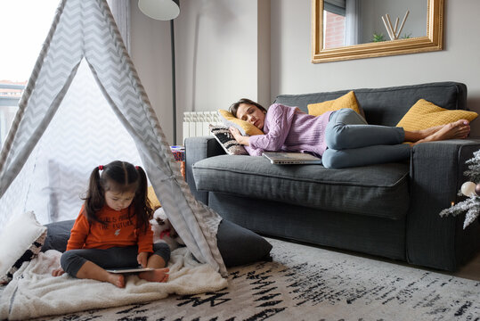 Ethnic girl browsing tablet near sleeping mother