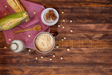 Fototapeta na wymiar Mazamorra cup with panela pieces, milk bottle and cobs over rustic wood table. Top of view of typical colombian drink, latin food concept. Copy space