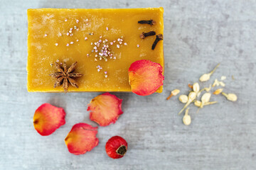 Handmade soap bar with rose petals, rosehip, jasmine, clove buds, anise star, and heather flowers on rustic wooden background. Aromatherapy and natural hygiene products concept. Space for text.