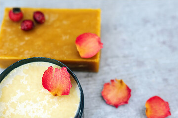 Handmade soap bar with rose petals, rosehips, and cocoa butter as a base for soap on wooden table. Spa photo on rustic background. Aromatherapy and natural hygiene products concept. Space for text.
