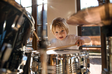 Front view of small boy indoors at home, playing drums.