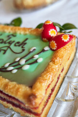 Homemade Mazurek, a very sweet flat cake baked for Easter in Poland. Polish Easter Cake decorated with sugar candy willow base, easter bunny, and eggs on a glass plate with periwinkle.