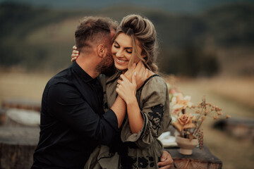 Close up portrait of a charming young couple laughing while man is embracing her wife outdoor in nature.